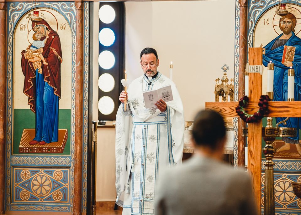 The Divine Liturgy at the iconostasis of the Church of the Archangels, the priest in white and blue vestments between icons of the Theotokos and Christ.